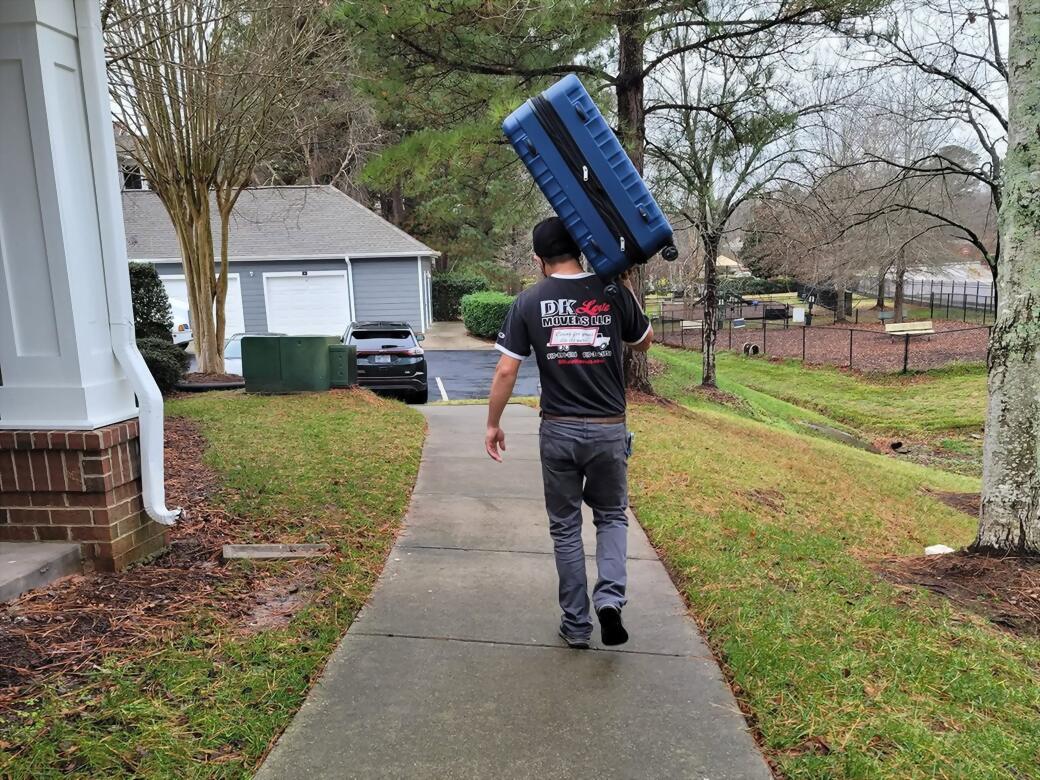 A DK Love Movers crew member carrying a wrapped case up the walkway to a customer’s home