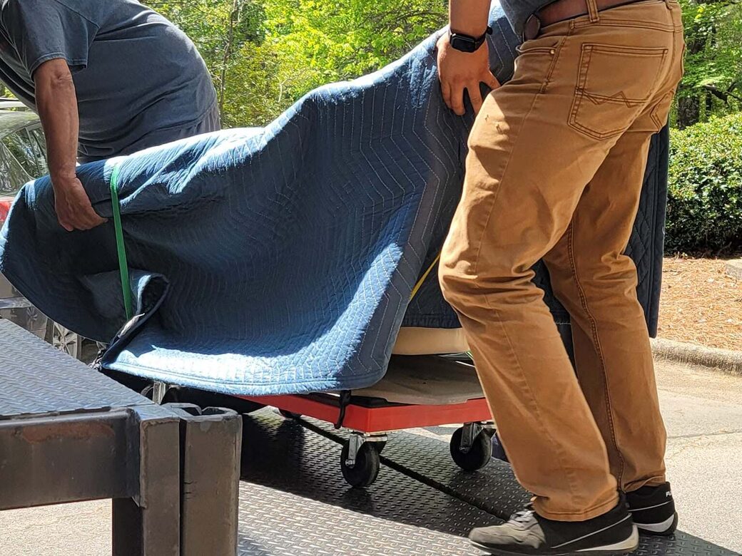 DK Love Movers crew guiding a blanket-wrapped piece up the truck ramp on a dolly